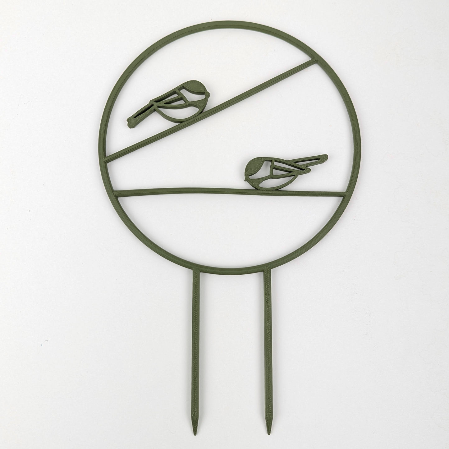 The chickadee trellis. A circle with two legs on the bottom for stakes. Across the middle are two branches running horizontally one on top of the other, each with a chickadee on it. Army Green colour against a white background.