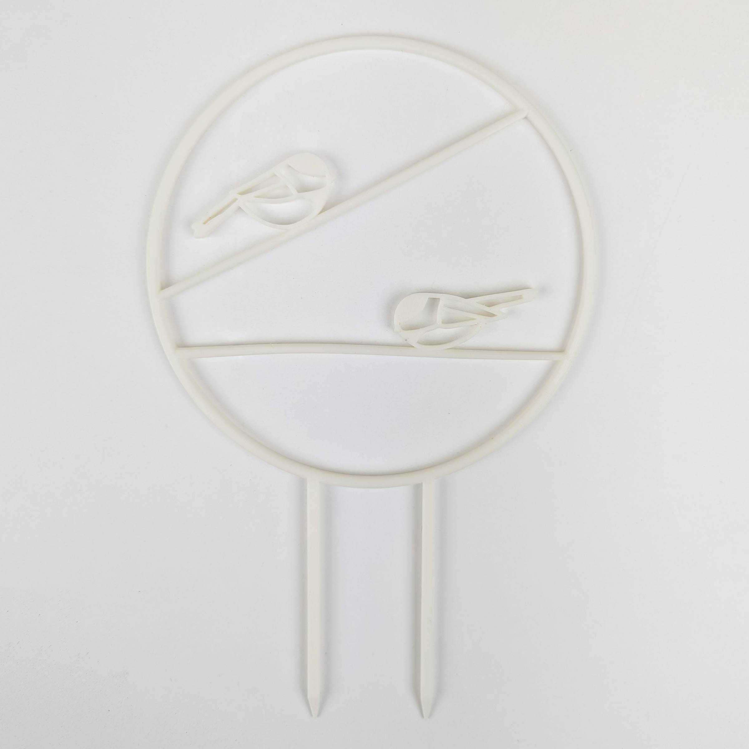 The chickadee trellis. A circle with two legs on the bottom for stakes. Across the middle are two branches running horizontally one on top of the other, each with a chickadee on it. White colour against a white background.