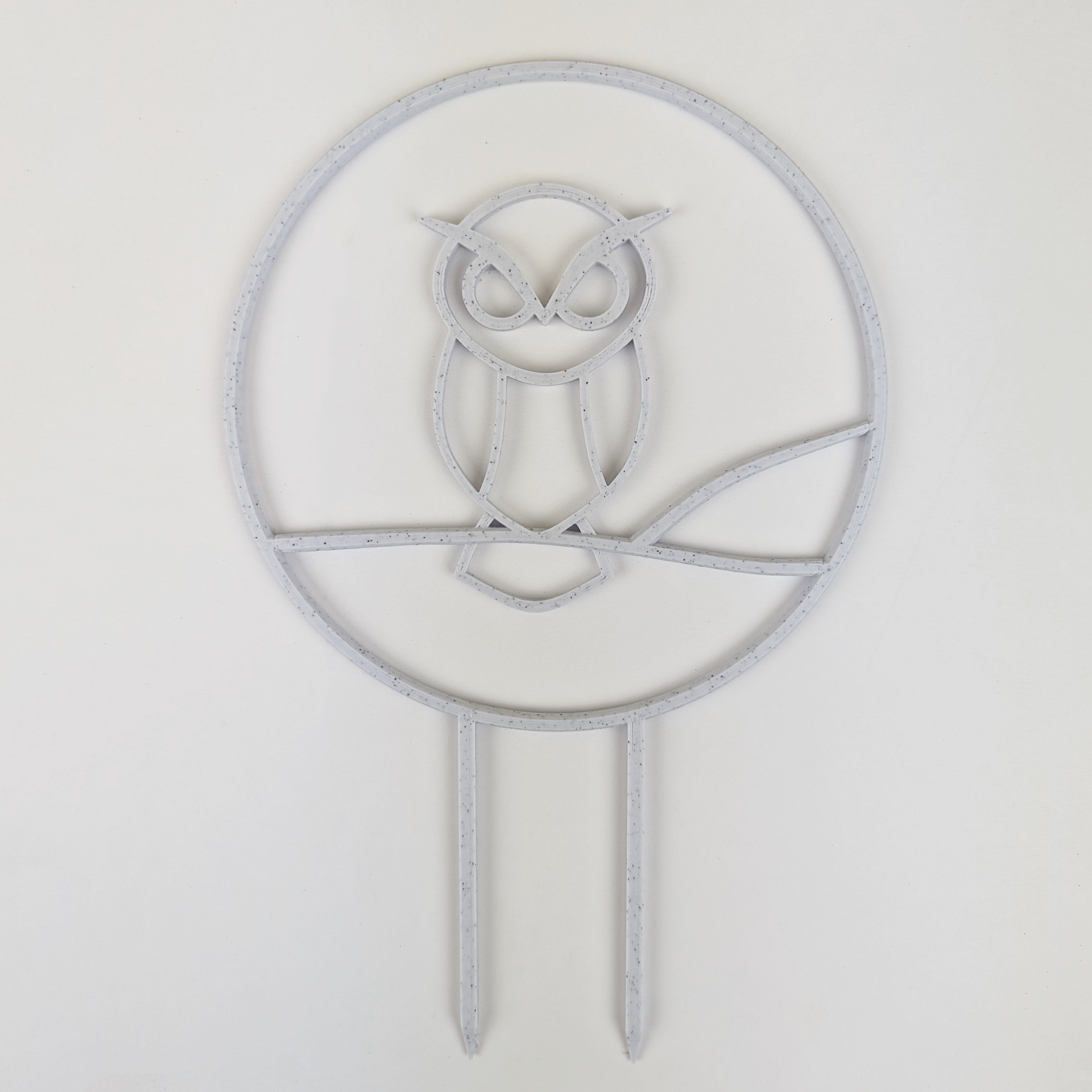 A circular trellis with an owl design in the middle. It is in the color marble