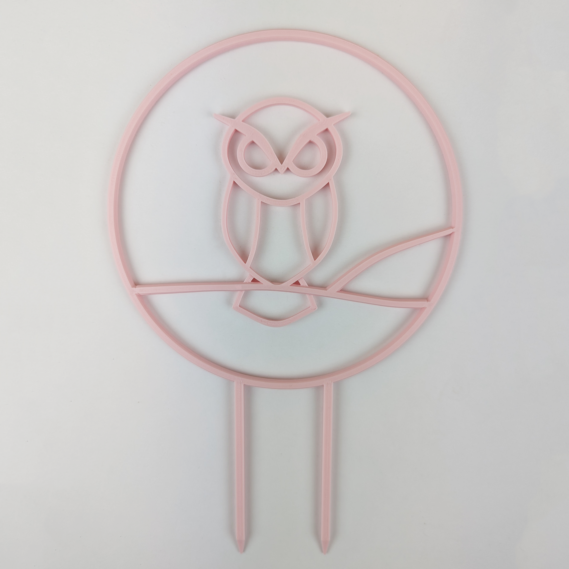 A circular trellis with an owl design in the middle. It is in the color pastel pink