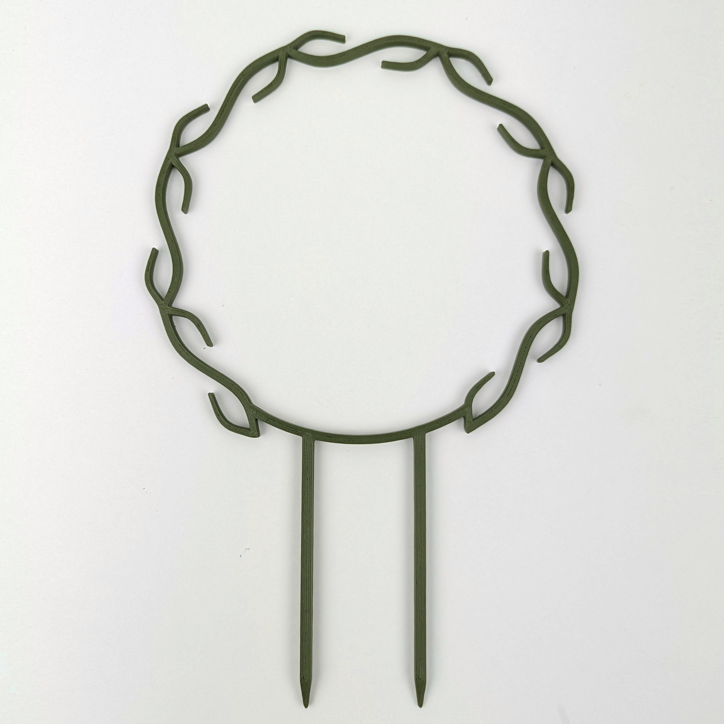 A wreath trellis. It has little hooks that go around in a circle, almost looking like a wreath. It is in dark army green colour against a white background.