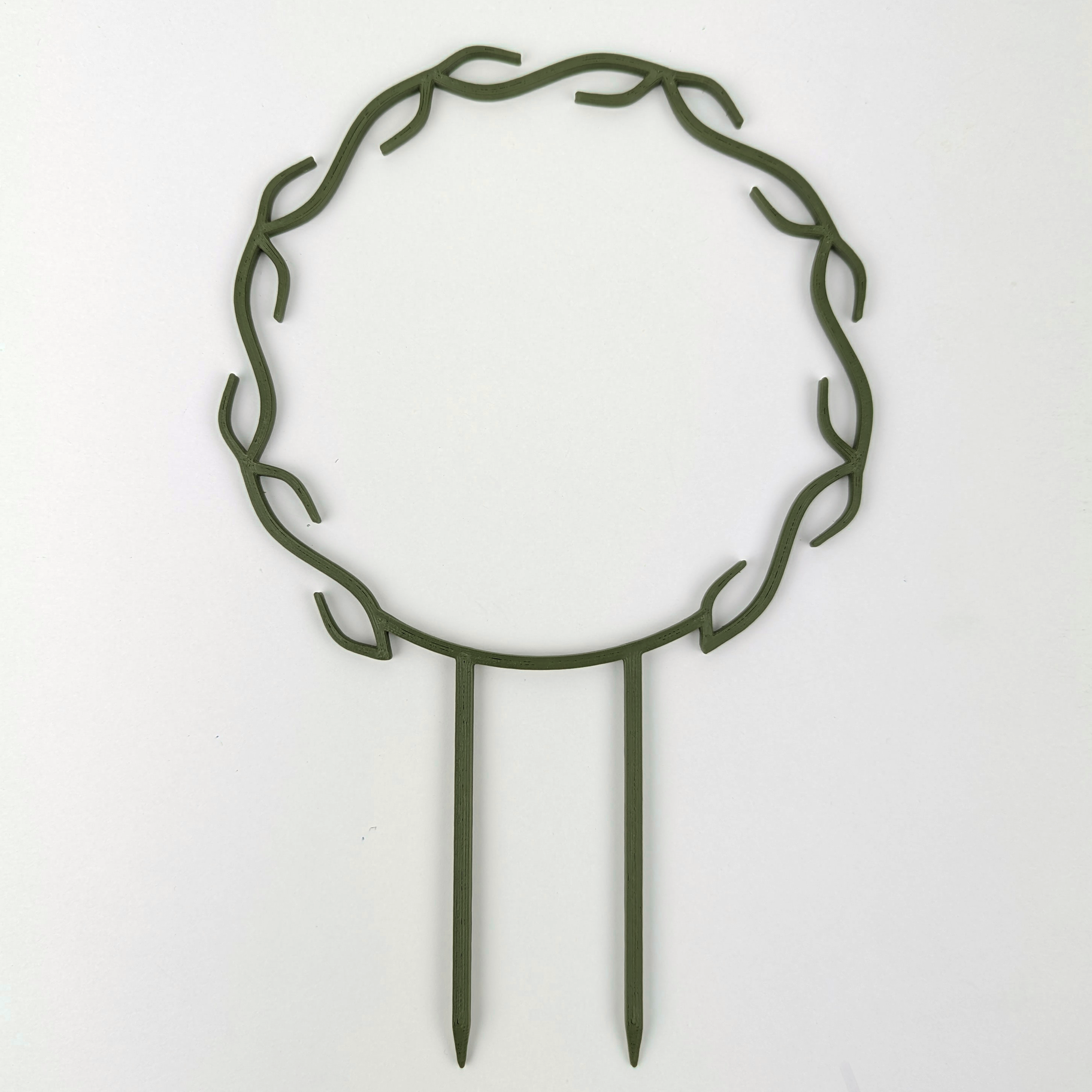 A wreath trellis. It has little hooks that go around in a circle, almost looking like a wreath. It is in dark army green colour against a white background.