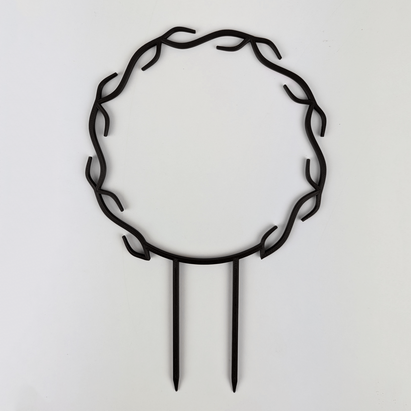 A wreath trellis. It has little hooks that go around in a circle, almost looking like a wreath. It is in black colour against a white background.