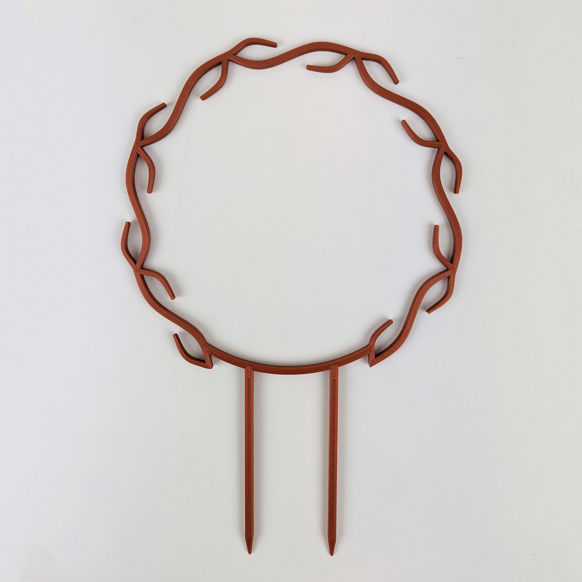 A wreath trellis. It has little hooks that go around in a circle, almost looking like a wreath. It is in copper colour against a white background.