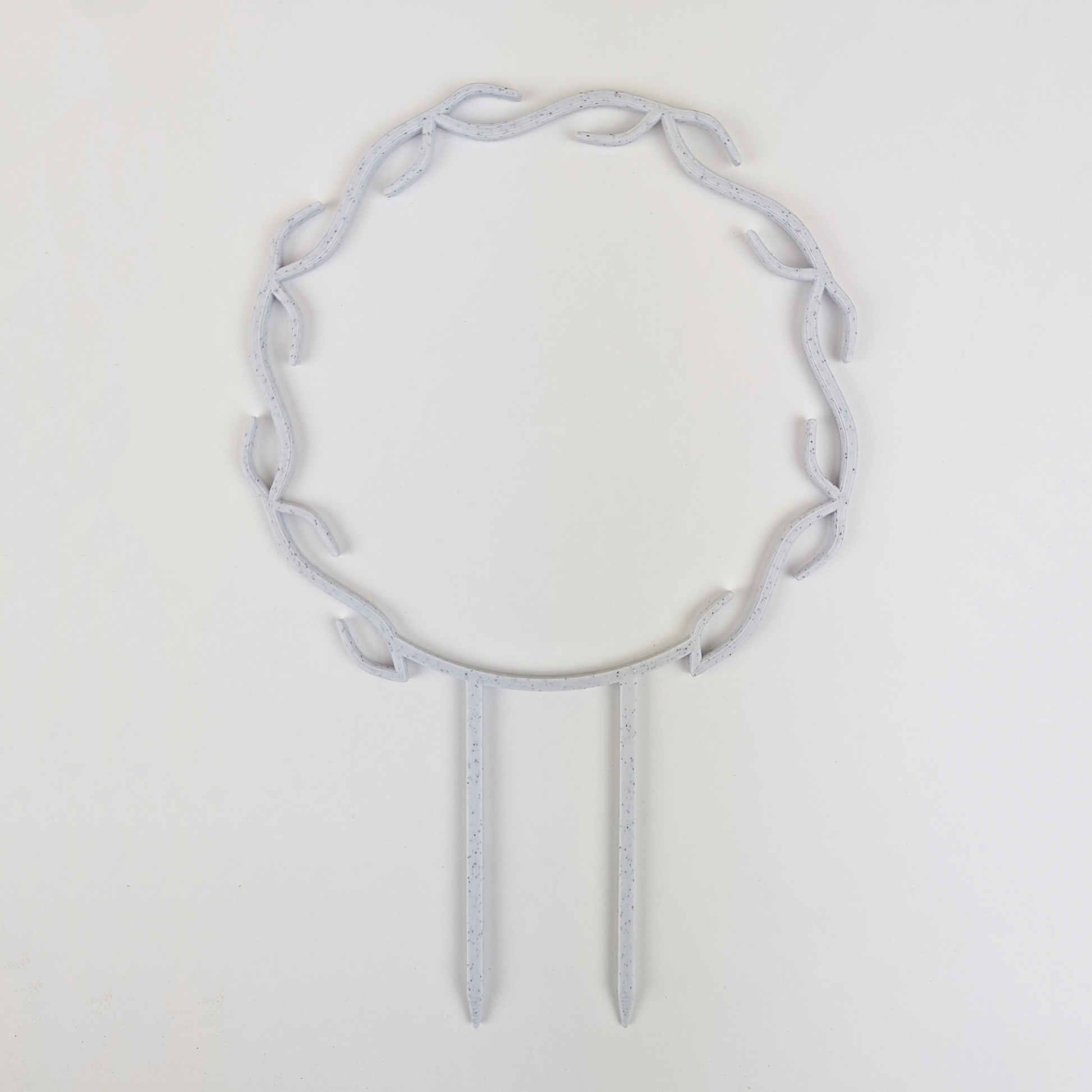 A wreath trellis. It has little hooks that go around in a circle, almost looking like a wreath. It is in marble colour against a white background.