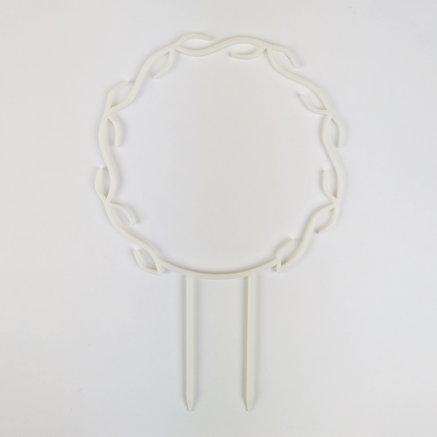 A wreath trellis. It has little hooks that go around in a circle, almost looking like a wreath. It is in white colour against a white background.